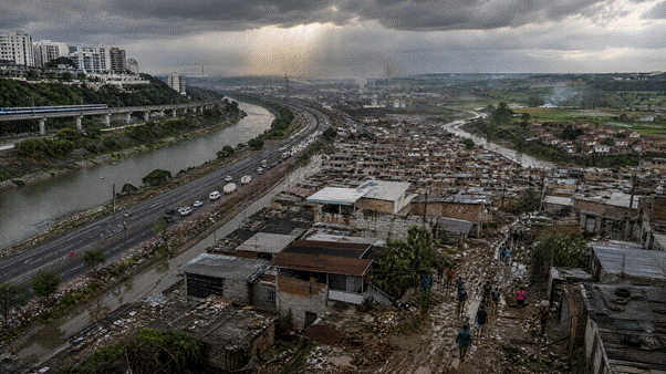 Cena representando a desigualdade territorial dos riscos ambientais: áreas privilegiadas com infraestrutura e proteção, comunidades vulneráveis sujeitas a enchentes e precariedade, zonas industriais e territórios rurais afetados pela poluição.